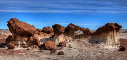 Unique rock formations with reddish-brown and white hues under a clear blue sky in a desert landscape.