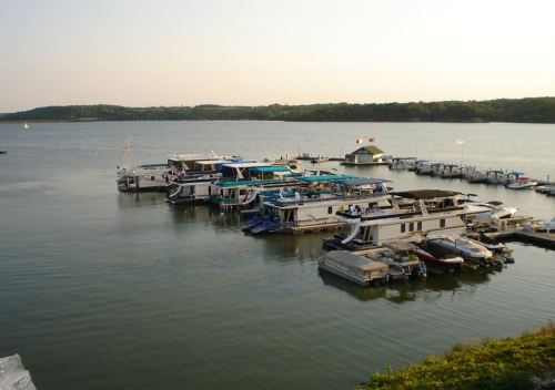A serene marina with several boats docked on calm water, surrounded by green hills under a clear sky.