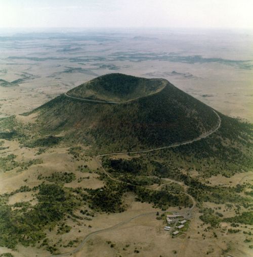 Aerial view of a volcanic crater surrounded by a vast, arid landscape with sparse vegetation.