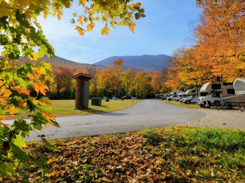 A scenic campground in autumn, featuring colorful foliage, a winding road, and parked RVs against a mountain backdrop.