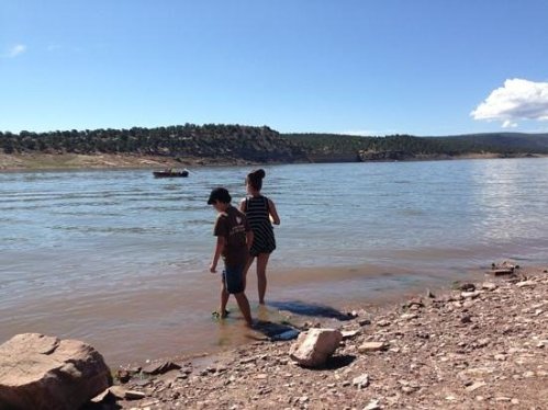 Two children play by the water's edge, with a scenic landscape and blue sky in the background.