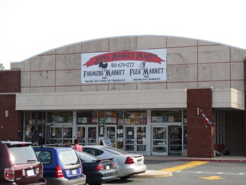 Exterior of a market building with a sign for a farmers and flea market, featuring parked cars in front.