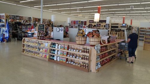 A spacious store interior featuring a central checkout counter with snacks and products, and shelves filled with goods.
