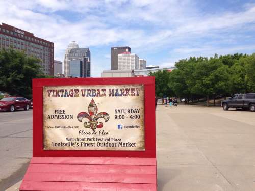 Sign for the Vintage Urban Market at Waterfront Park, Louisville, with city skyline in the background. Free admission.