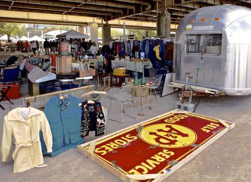 A bustling outdoor market with vintage items, clothing, and an Airstream trailer under a bridge.
