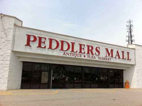 Exterior of Peddlers Mall, an antique and flea market, featuring a large sign and glass entrance.