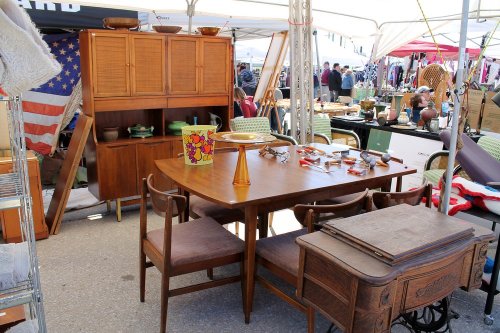 A vintage furniture display at a market, featuring a wooden dining table, chairs, and various decorative items.