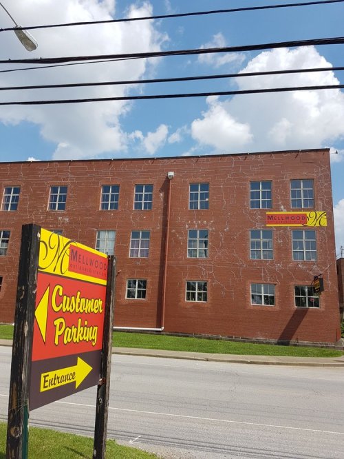 A brick building with a sign for Melwood and a customer parking entrance, under a blue sky with clouds.