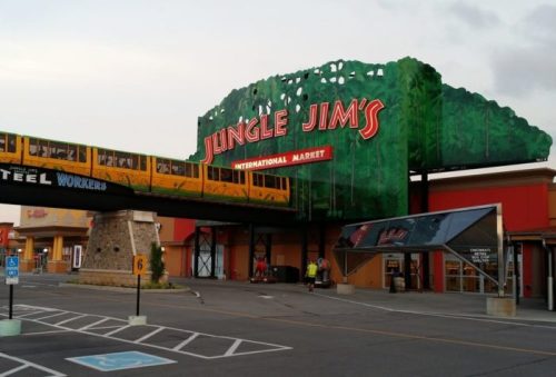 A colorful sign for Jungle Jim's International Market with a train overhead and a parking lot in front.