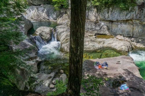 A serene river scene with a small waterfall, rocky banks, and a picnic setup on a flat stone surface.