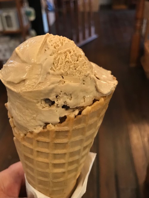 A close-up of a cone filled with creamy brown ice cream, held in a hand, with a rustic wooden background.