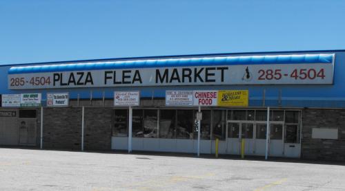 Exterior of Plaza Flea Market with a blue roof and various signs, including a Chinese food advertisement.