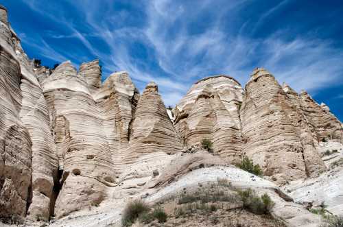 Layered rock formations rise against a blue sky with wispy clouds, showcasing natural erosion patterns.