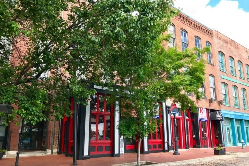 Historic brick buildings with red accents and greenery in the foreground, set against a blue sky.