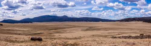 A panoramic view of a vast, dry landscape with rolling hills and a blue sky filled with fluffy clouds.