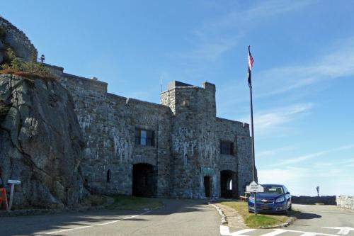 Stone castle with a flagpole and a parked car, set against a clear blue sky.