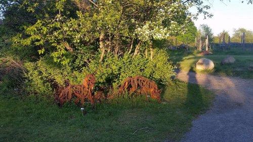 Two rusted metal sculptures of horses nestled among green bushes in a sunny outdoor setting.