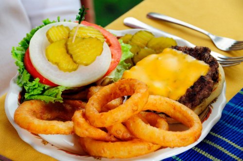 A plate featuring a cheeseburger with lettuce, tomato, onion, pickles, and a side of crispy onion rings.