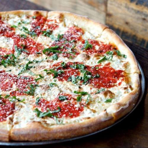 A freshly baked pizza topped with tomato sauce, mozzarella cheese, and fresh basil on a wooden table.