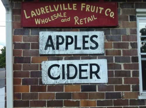 Sign for Laurelville Fruit Co. featuring "Apples" and "Cider" on a brick wall.