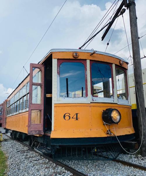 Vintage orange streetcar numbered 64, parked on tracks with cloudy sky in the background.
