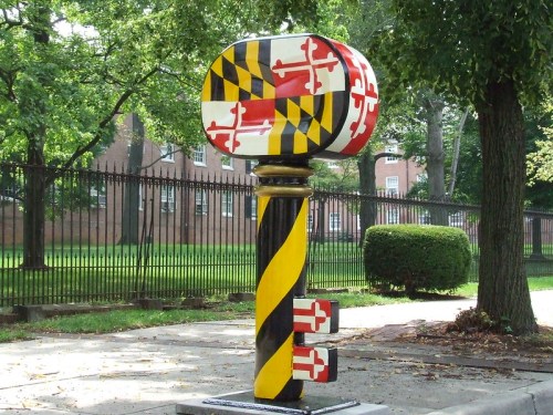 Colorful Maryland-themed mailbox featuring the state flag design, set in a park-like area with trees.