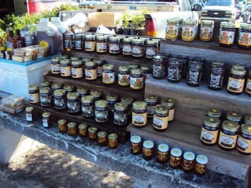 A display of various jars of honey and preserves arranged on wooden shelves at a market.