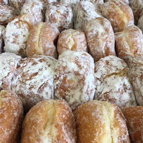 A close-up of a pile of powdered sugar donuts, showcasing their fluffy texture and sweet coating.