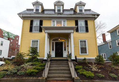 A large yellow Victorian-style house with a front porch, black shutters, and landscaped gardens.