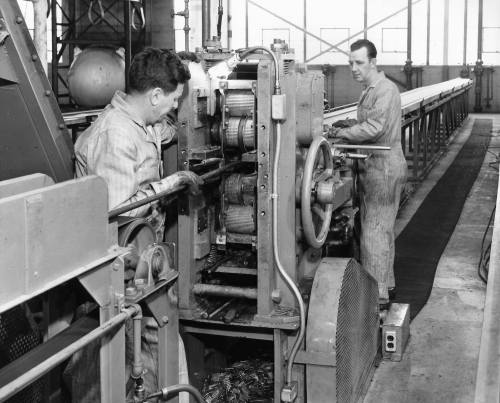 Two workers operating machinery in a factory, focused on their tasks amidst industrial equipment.