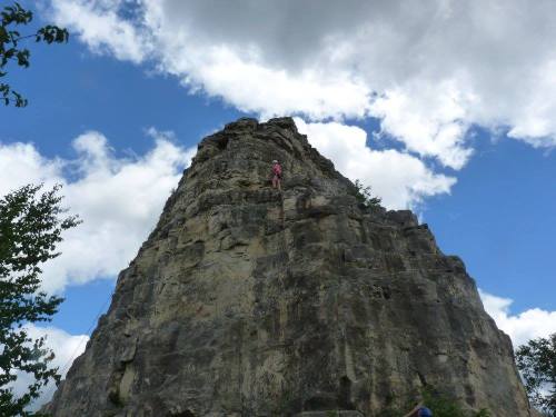 A tall rock formation under a cloudy blue sky, with a person climbing near the top.