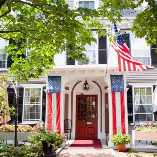 A charming house with a red door, American flags, and lush greenery in a welcoming front yard.