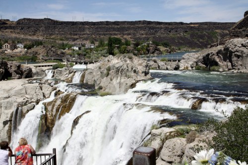 A scenic view of a waterfall cascading over rocky cliffs, surrounded by greenery and a distant landscape.