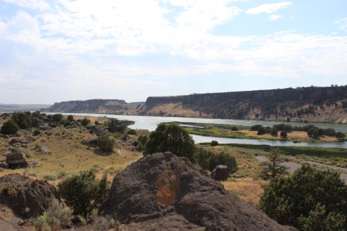 A scenic view of a river winding through rocky terrain and hills under a partly cloudy sky.