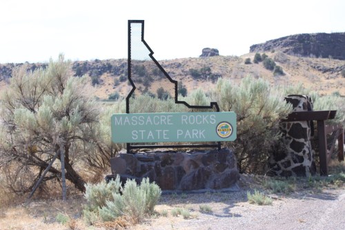 Sign for Massacre Rocks State Park in Idaho, featuring a silhouette of the state and surrounded by shrubs.