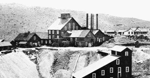 Historic black-and-white photo of a mining facility with multiple buildings and smokestacks in a mountainous landscape.