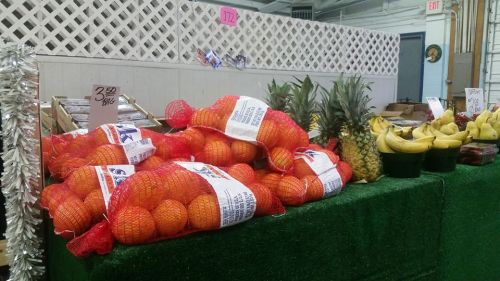 Bags of oranges and pineapples on a green table, with bananas and other fruits in a market setting.