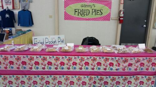 A table displaying various fried pocket pies, with a sign reading "Gammy's Fried Pies" in a colorful setting.