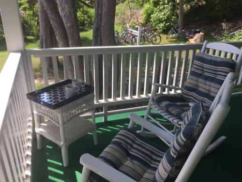 A cozy porch with two striped rocking chairs and a small table, surrounded by greenery and bicycles in the background.