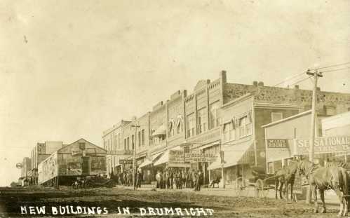 Historic street scene in Drumright, featuring new buildings, storefronts, and people gathered outside.