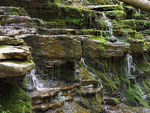A serene rocky landscape with cascading water and lush green moss covering the stones.