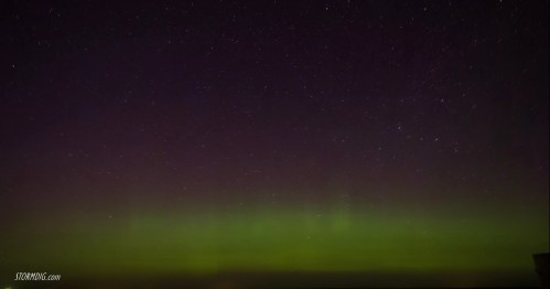 A night sky filled with stars, featuring a vibrant green aurora borealis illuminating the horizon.
