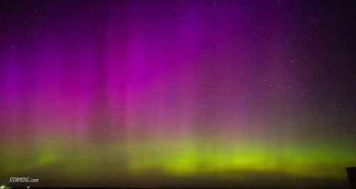 Vibrant aurora borealis with purple and green hues illuminating the night sky, dotted with stars.