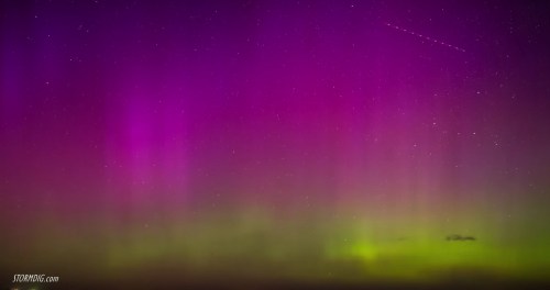 A vibrant display of purple and green auroras against a starry night sky.
