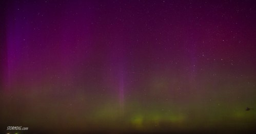 A vibrant display of purple and green auroras against a starry night sky.