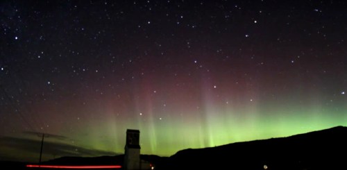 A stunning night sky featuring vibrant auroras and a starry backdrop over a dark landscape.