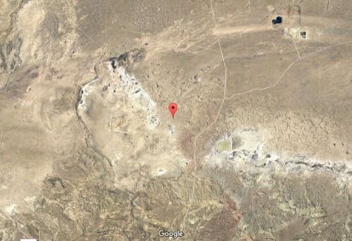 Aerial view of a barren landscape with a red pin marking a specific location on a map.