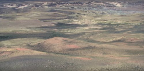 Aerial view of a vast, arid landscape with rolling hills and sparse vegetation under a clear sky.
