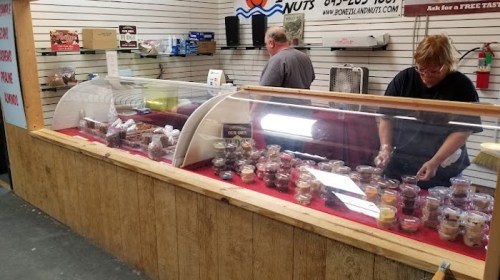 Two employees work behind a display case filled with various desserts in a shop with a wooden counter.