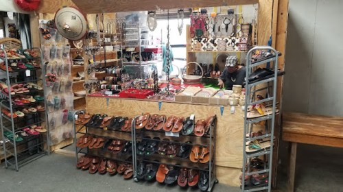A wooden display featuring various shoes and jewelry, with a vendor organizing items in a market setting.